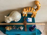 Overview of seven cat figurines including two large pieces in the back and five smaller ones in front with a ruler for scale