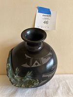 Front view of the black clay vase showing attached green iguana and geometric etched designs