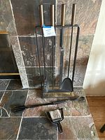Full view of stand with hanging tools on tile hearth plus separate tongs and hand brush on floor