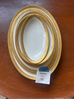Five nested oval porcelain platters with wide gold ornate borders displayed on wood surface.