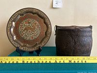 Photo of metal plate and carved wood container side by side with measurement tape showing size.