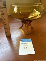Side view of amber glass bowl measuring approximately 4.5 inches in height, showing three curved legs.