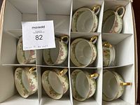 Set of 10 Union K tea cups and saucers arranged in box compartments, showing gold handles and floral patterns on cups and saucers.