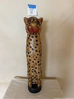 Full view of tall, slender, hand-carved wooden cheetah sculpture with painted spots, cross patterns and red painted cheeks.