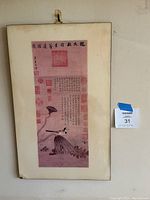 Full image of framed Asian calligraphy and lotus pond art with red seals, mounted behind glass in a simple frame with hook.