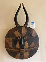 Front view of the wood carved African mask showing the full circular face, intricate geometric patterns, and tall curved horns.