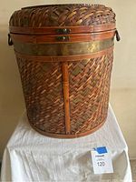 Closed view of large woven basket showing metal band and handles, with natural reed material in warm brown tones