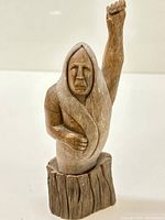Full view of the Inuit wooden carving on its base showing the figure with one arm raised.