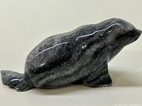 Side profile view of the polished grey stone carving of a seal, showing its tail, body contours, and texture.