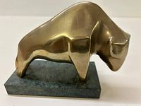Front view of a smooth, angular brass bull figurine on a green marble rectangular base, showing profile and size reference.