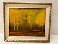 Framed oil painting depicting a forest scene with trees and bright yellow foliage in a gold and cream frame.