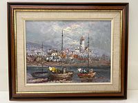Framed oil painting showing a harbor scene with two sailboats near a town with a tower.