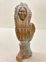 Front view of the carved Inuit figure showcasing the elderly face, feathered headdress, and portion of the attire.
