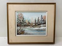 Framed oil painting showing a winter scene with snow-covered trees and a river, signed by the artist at the lower right.