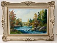 Framed oil on board painting showing a river running through a forest with autumn-colored trees under a blue sky.