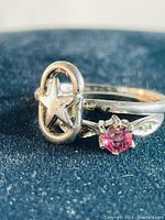 Close-up photo of sterling silver star logo ring and pink garnet ring on black surface