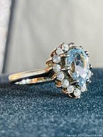 Side angle photo showing the pear-shaped aquamarine stone held by prongs with clear stones halo and sterling silver band.