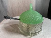 Side view of the Fenton jadeite sugar bowl with green lid and clear textured body, showing the spoon inserted through the lid slot.
