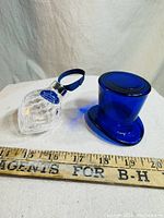 Two items shown side by side with measuring stick: clear heart-shaped crystal ornament with blue ribbon and separate cobalt blue crystal top hat form.