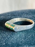 Close-up photo of sterling silver ring with green inlay stone, possibly jade. Shows matte silver band and rectangular top with inlaid stones.