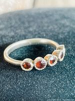 Close-up side angle of sterling silver ring with five round red stones, possibly garnets, bezel set on a silver band.
