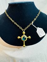 Front view of gold-tone cross pendant with central blue Murano glass on a gold-tone chain displayed on a black necklace stand.