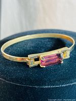 Close up photo of vintage Avon gold tone bracelet showing rectangular purple stone and part of bracelet band