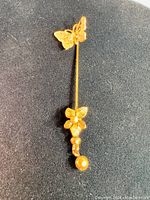 Full view of the vintage gold-tone butterfly and flower pin laying on a black surface showing its design and length.