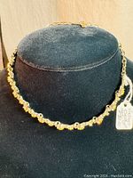 Full view of the vintage CORO necklace displayed on a black stand showing the yellow stones and gold-tone metal.