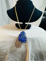 Full view of the gold-tone chain necklace displayed on a black jewelry bust with carved blue stone pendant attached.