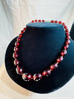 Full view of the vintage facetted Bakelite beaded necklace displayed on black bust showing the rich red color and bead size graduation.