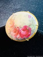Top view of oval hand painted porcelain brooch showing pink and red rose design.