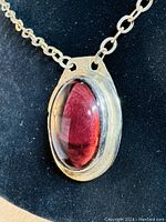 Close-up of the front of the pendant showing deep red oval Murano glass cabochon and silver-tone metal setting.
