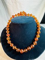 Full view of the 28-inch vintage cognac amber large clear beads necklace displayed on black stand.