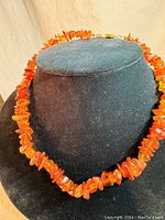 Full view of the shorter raw amber choker necklace on display stand, showing the bright orange irregular beads and clasp.