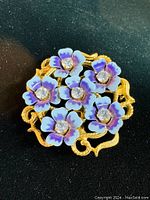 Front angled photo of the vintage AVON floral pin pendant, showing purple enamel petals with rhinestone centers on a gold-tone metal base.