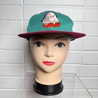 Front view of teal and maroon baseball cap with embroidered Grumpy face on front