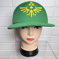 Front view of green baseball cap on mannequin head showing the yellow Legend of Zelda emblem.