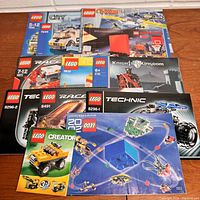 Top-down photo showing all 10 Lego instruction books/catalogs spread out on a wooden floor, showcasing various themes and brightly colored covers.