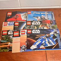 Top view of the 7 visible Lego Star Wars instruction booklets laid out on a wood floor showing the front cover with colorful Lego Star Wars images and set numbers.