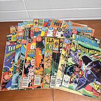 Photo of 22 comic books spread out showing covers with titles including Spider-Woman, Teen Titan, Legion, and others.