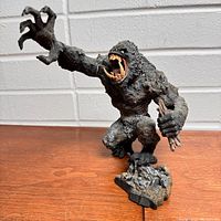 Front view of the detailed McFarlane CONAN Man Eating Hunter figure showing the open mouth, extended clawed hand, and sticks in another hand, mounted to rock base.
