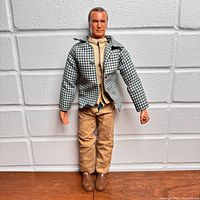 Front view of Oscar Goldman action figure standing against a textured wall, showing full body with clothing and molded brown shoes.