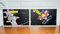 Two Star Wars comic style posters displayed side by side on a table against a white brick backsplash. The left poster shows an X-Wing firing lasers in space, the right poster shows a TIE Fighter explosion with 'WHAAM!' text.