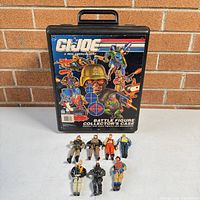 Closed view of vintage black plastic G.I. Joe Battle Figure Collector's Case with original colorful front art, and 7 G.I. Joe action figures arranged below.