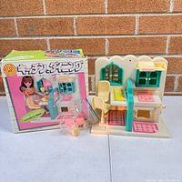 Front view of vintage Japanese doll kitchen playset alongside original box and small pink plastic accessories.