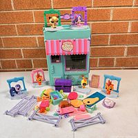 Front view of the Littlest Pet Shop plastic store case with six pet figures and multiple small accessories arranged in front on a white surface.