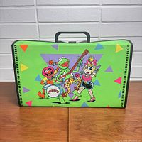 Front side of neon green storage case featuring colorful triangles and graphic of Muppets characters Animal, Kermit, and Miss Piggy.