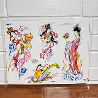 Full view of tattoo flash art sheet with four Asian-inspired figures amid colorful clouds and a bird, sealed in lamination.