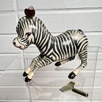 Front diagonal view of the vintage tin wind-up zebra toy showing the detailed stripes, facial features, and attached metal key.